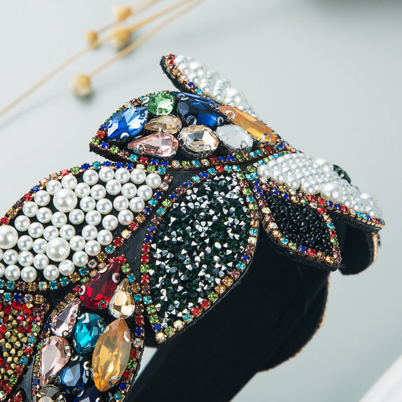 Wide rhinestone headband with white pearl petals and blue-green gem leaf details