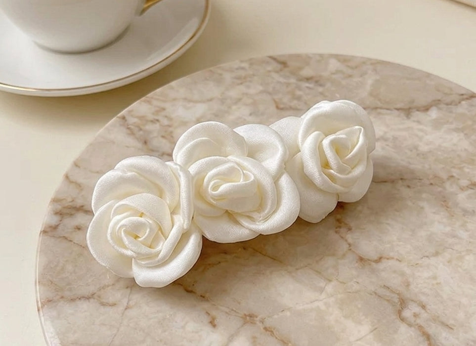 White satin rose clip-on barrette with three fabric rosettes, side view.