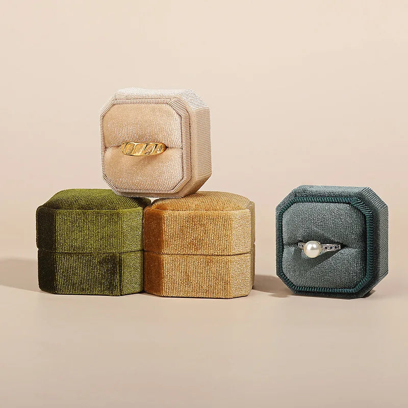 Octagonal velvet ring box set in olive, tan, and teal with open lid rings