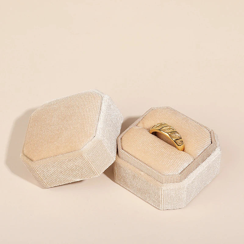 Beige octagonal velvet ring box set, open lid showing a gold ring