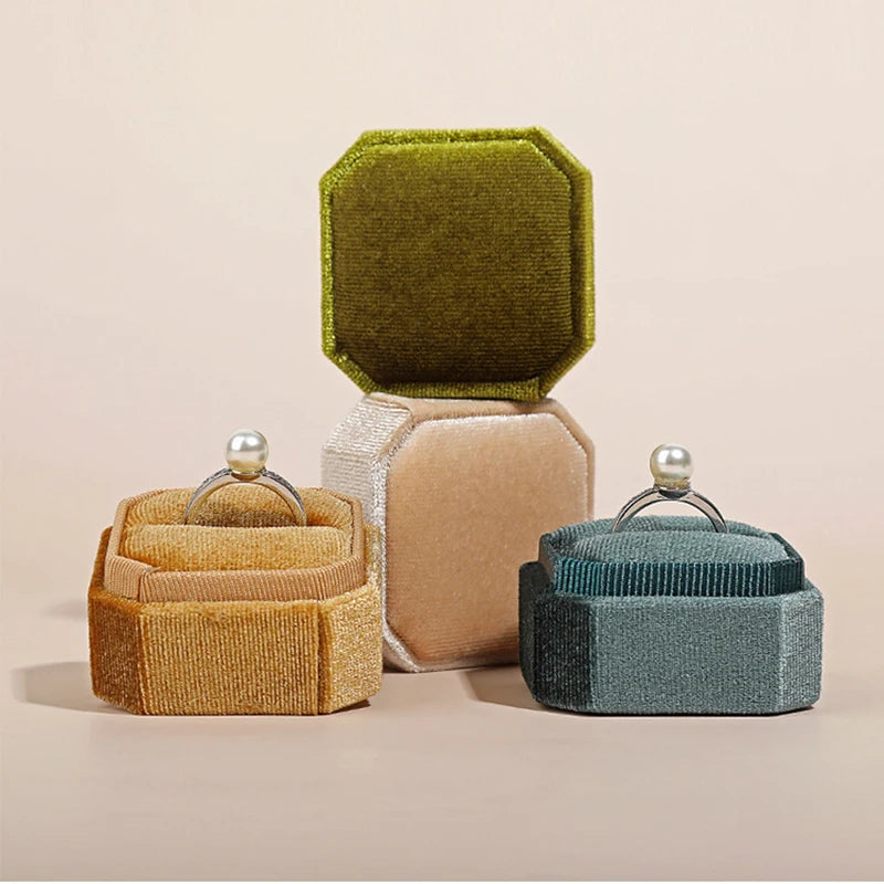Octagonal velvet ring boxes with open lids: olive, tan, and teal colors