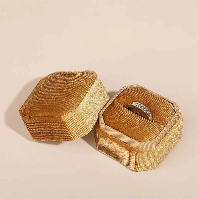Gold and tan octagonal velvet ring boxes open, with a ring in the tan box