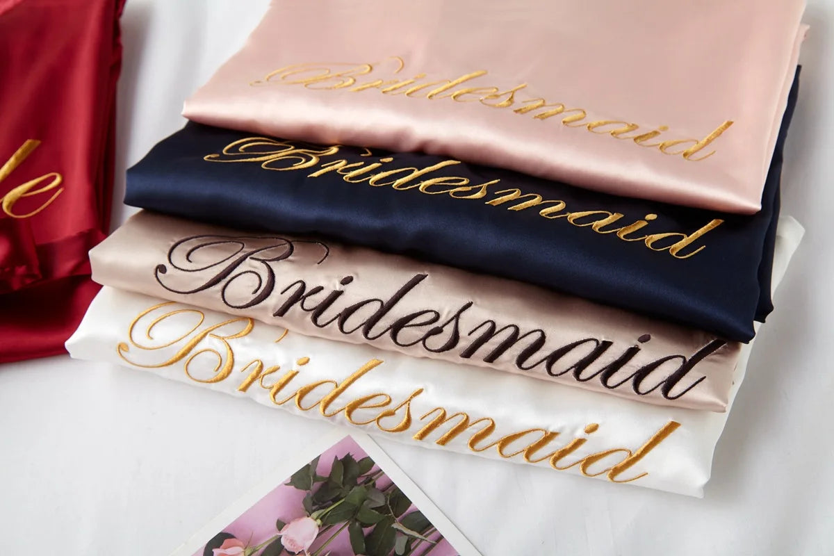 Close-up of satin robes with embroidered Bride and Bridesmaid text in light colors