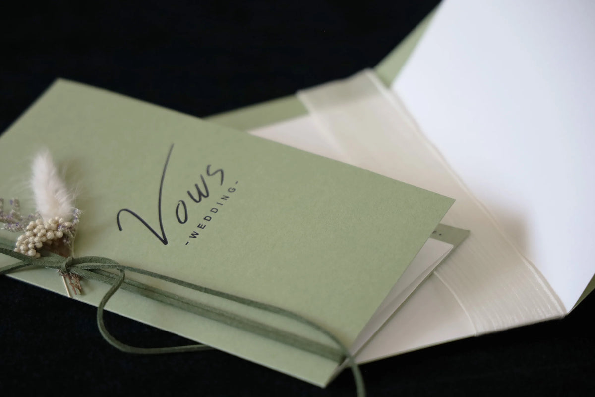 Sage wedding vows booklet with feather detail on cover and open pages behind
