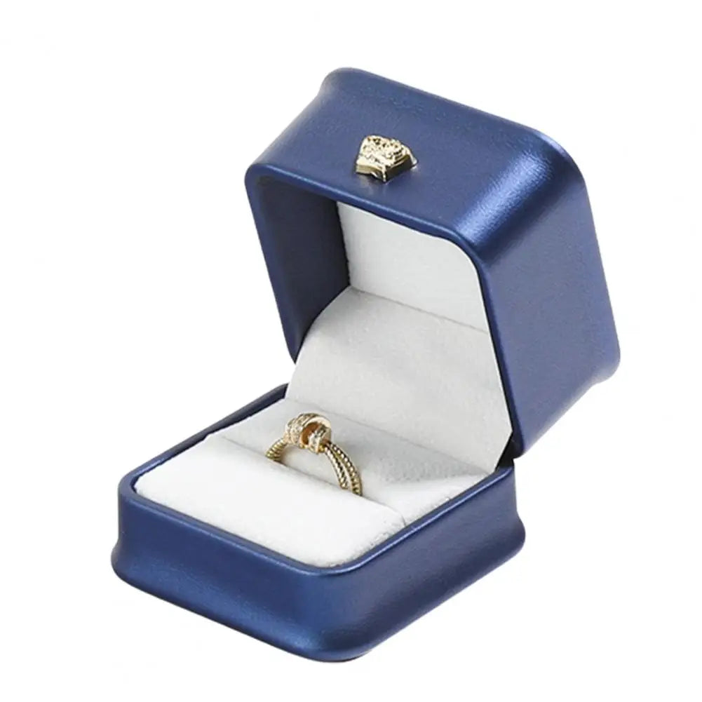 Blue ring box with gold crown clasp, open lid, and ring on white cushion