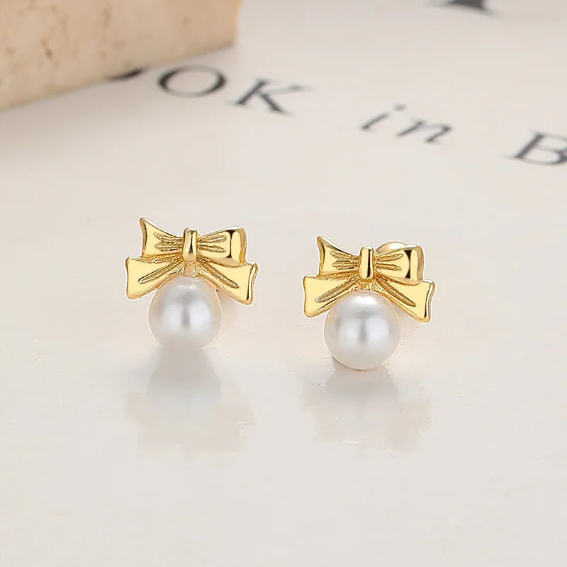 Gold bow stud earrings with white pearl drop, ball posts