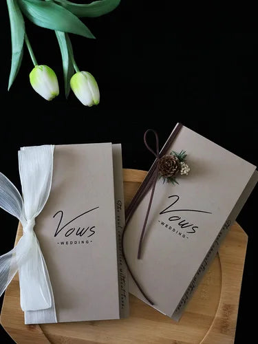Ivory vows booklet set with gold foil vow text, dried floral decor, and white ribbon ties
