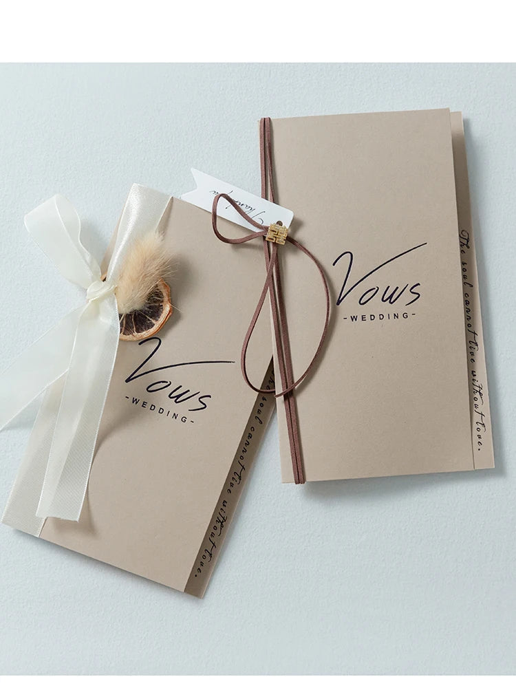 Ivory vows booklets with gold-foil “Vows Wedding,” tied with white ribbon bows and ribbon loops