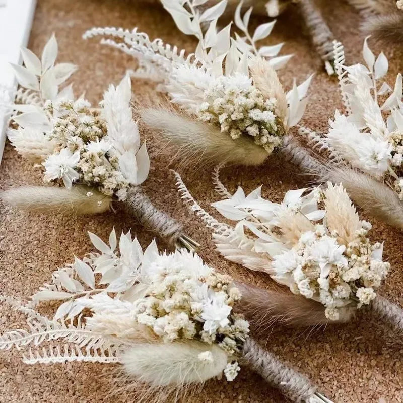 Assorted dried flower boutonnieres with white feathers, cream blooms, and twined stems