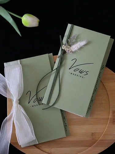 Ivory vows booklet set with gold foil vow text, floral pin, and wrapped ribbon
