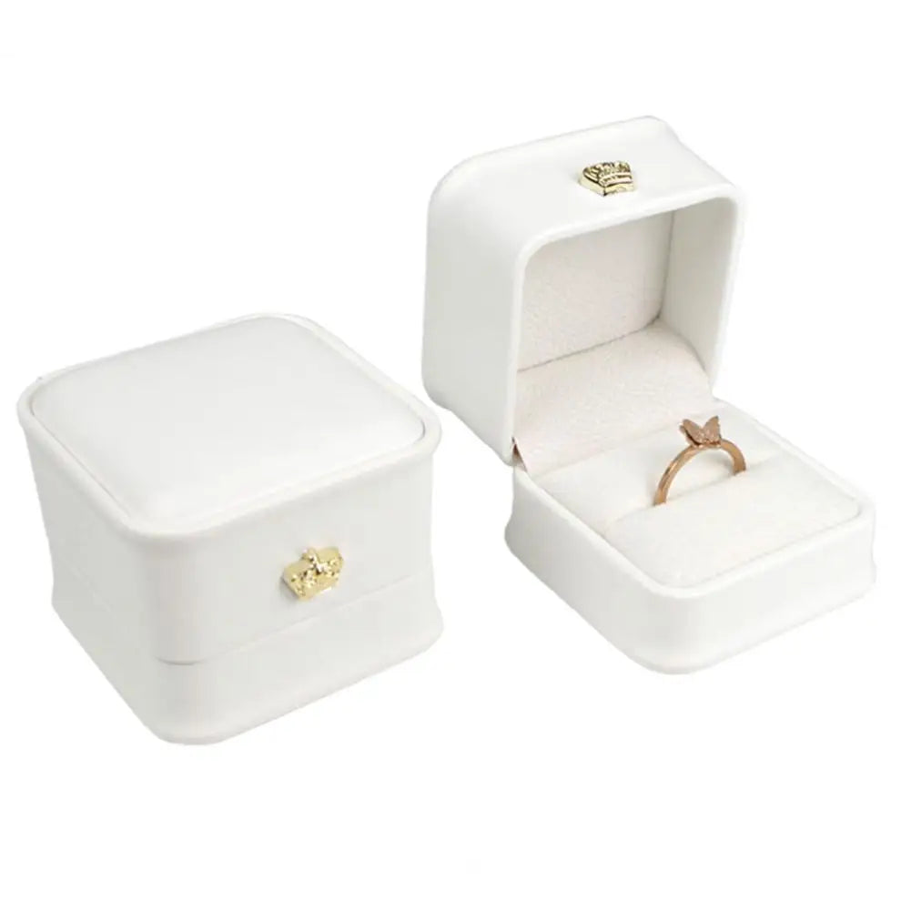 White ring box set with gold crown clasp and ring on white foam cushion