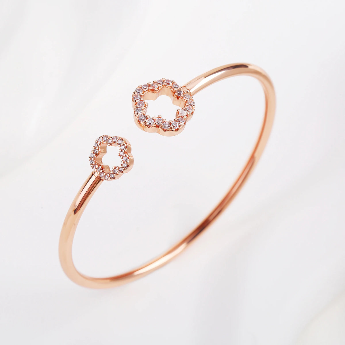 Rose gold open cuff bangle with two zirconia clover charms, one close-up center