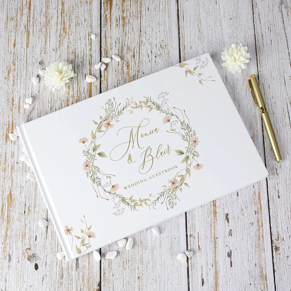 Wedding guest book with floral wreath cover, personalized names, angled view, white with gold details