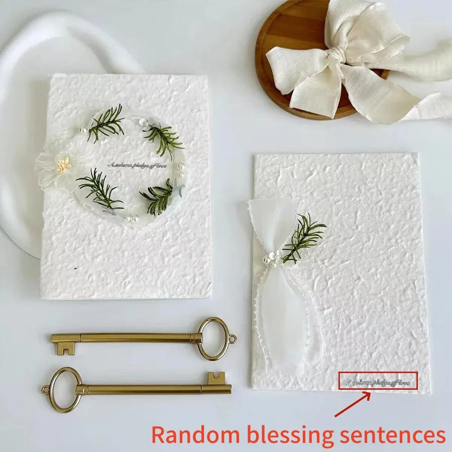 White wedding vow booklets with sage ribbon ties, green fern heart wreath, and pearl details
