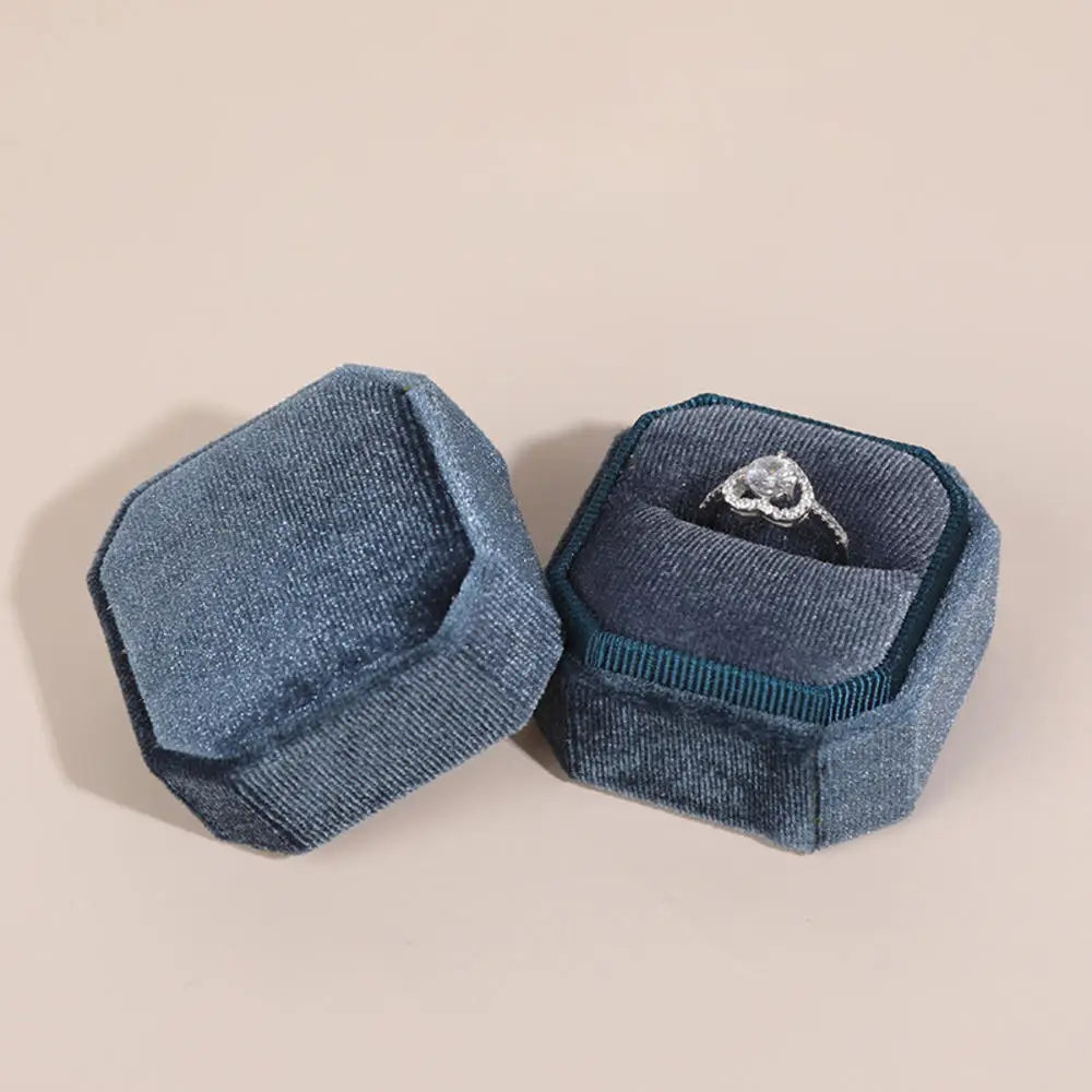 Blue octagonal velvet ring boxes open with a silver ring inside