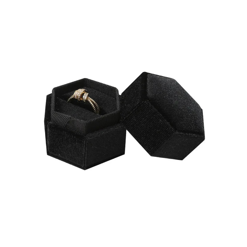 Black octagonal velvet ring box set with open lid and gold ring inside