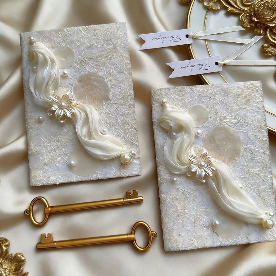 Pair of white wedding vow booklets with embossed feather/floral embellishments and pearl trim