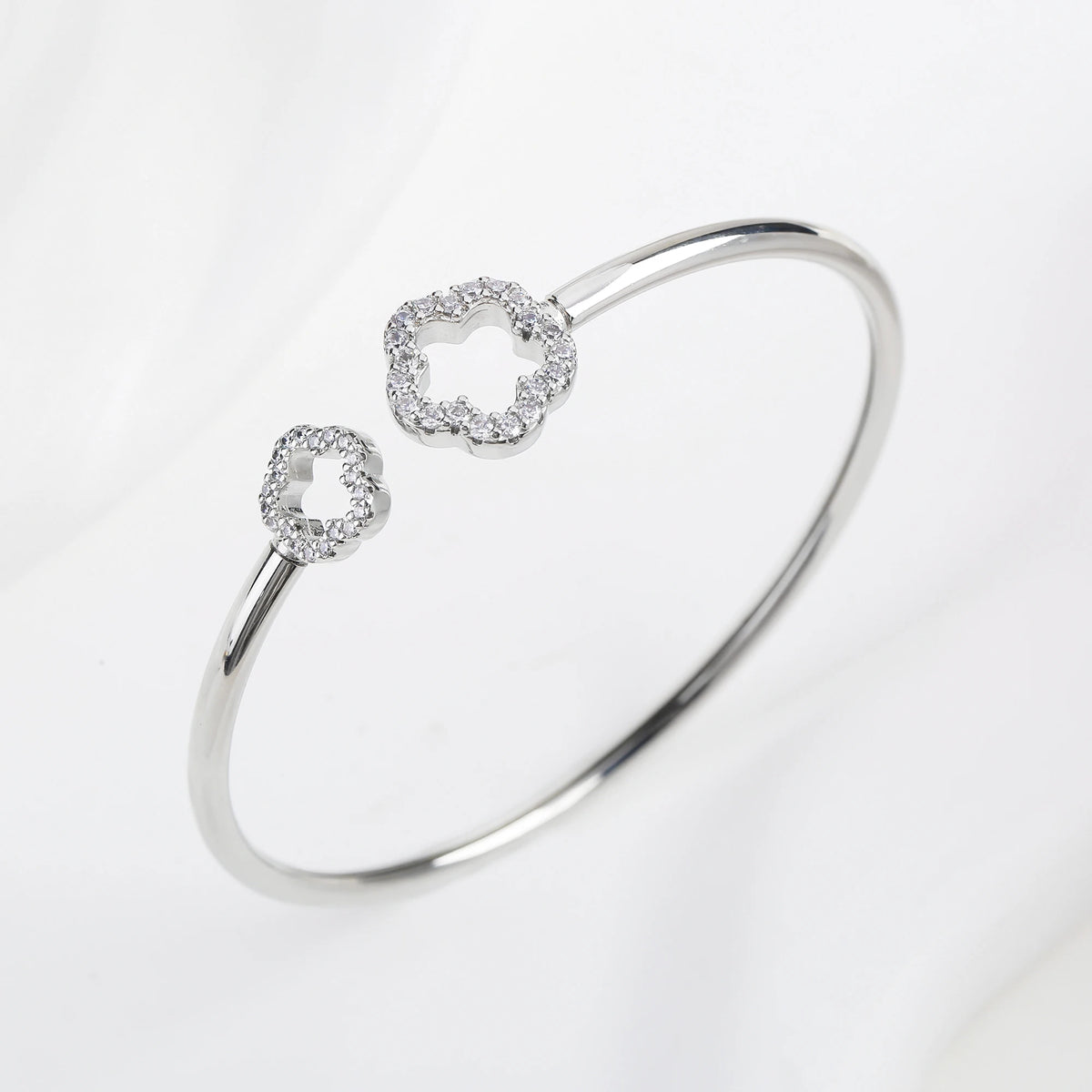 Silver open cuff bangle with two zirconia clover charms and a glossy open oval band