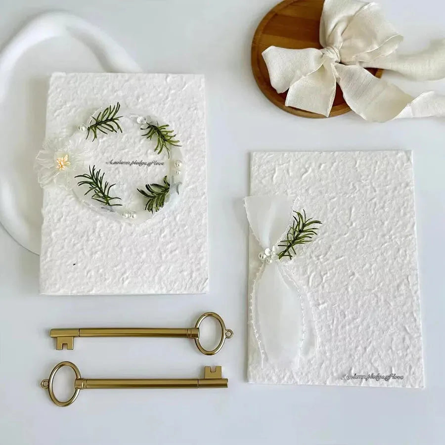 White wedding vow booklets with green fern wreath heart, white ribbon ties, and pearl detail