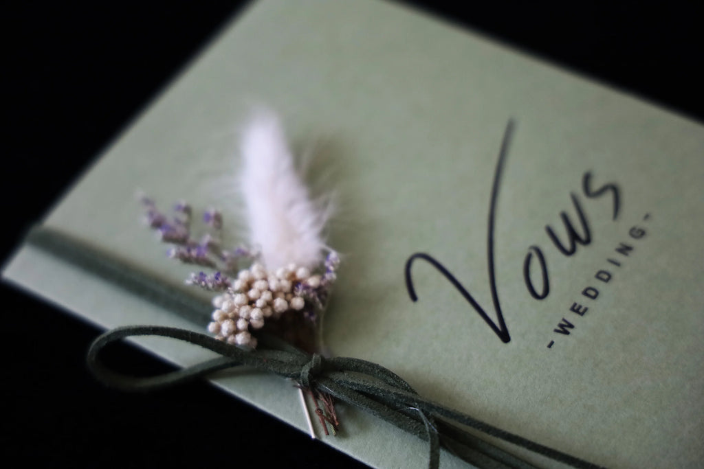 Close-up of sage wedding vows cover with feather and pearl floral bow decoration