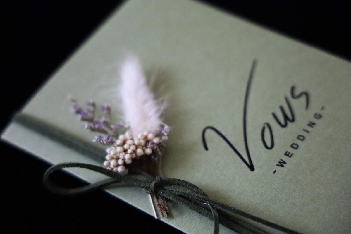 Close-up of sage wedding vows cover with feather and pearl floral bow decoration