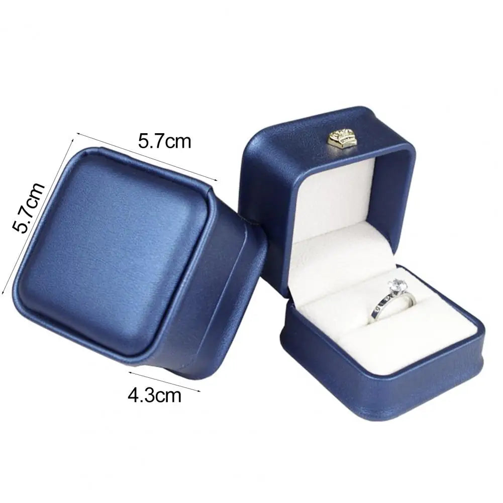 Blue ring box with open lid and size measurements, gold crown clasp and ring cushion