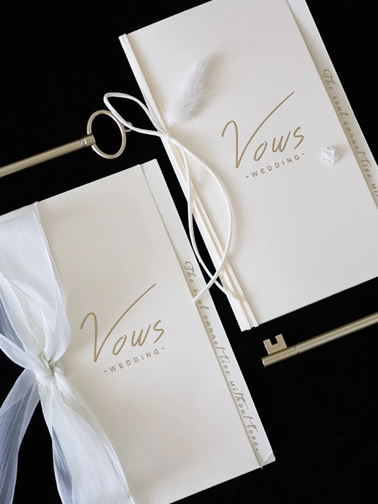 Ivory wedding vow booklet with gold foil “Vows,” white ribbon and metal clip detail