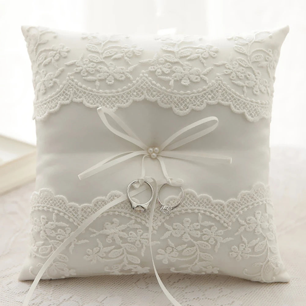 White ring bearer pillow with lace trim, bow, and small ring holder at center
