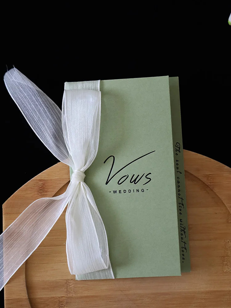 Sage green wedding vows booklet with white ribbon bow and gold-toned text