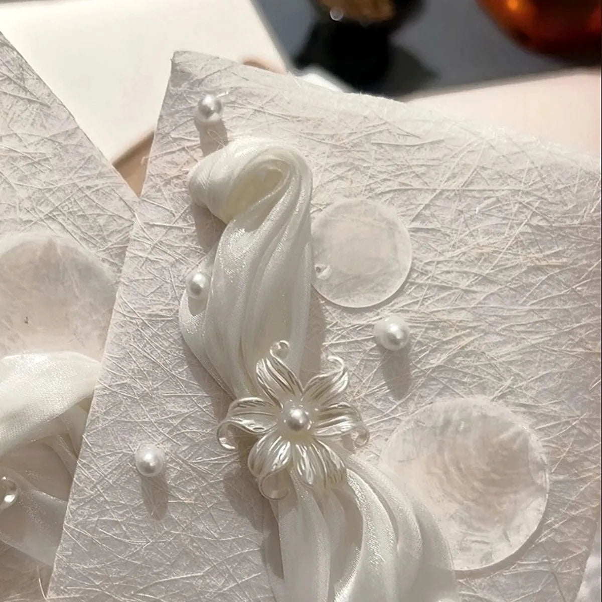 White textured wedding vow booklet with sheer ribbon, pearl trim, and flower centerpiece