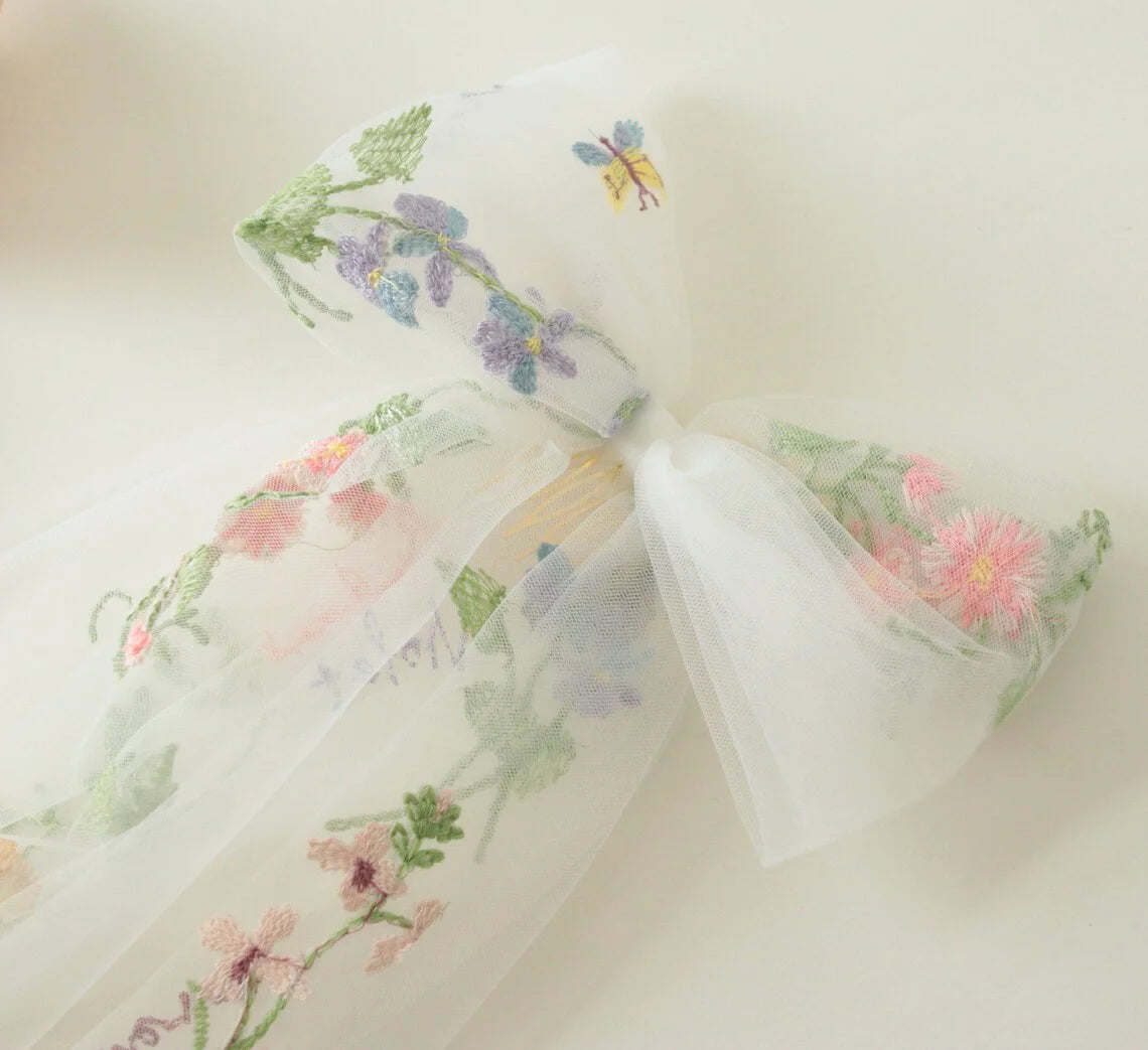 White tulle hair bow with embroidered floral and butterfly details and sheer tails