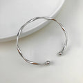Silver twisted ribbon sculptural cuff bracelet with two ball ends