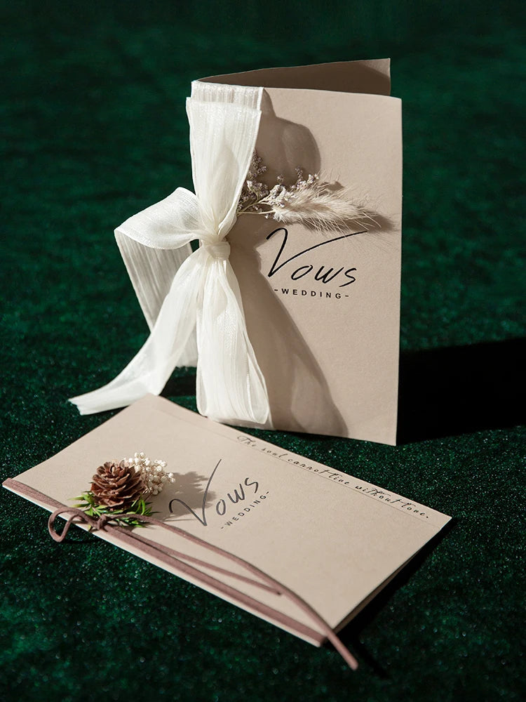 Ivory vows booklet set with gold-foil lettering, white ribbon bow and pinecone-style accents