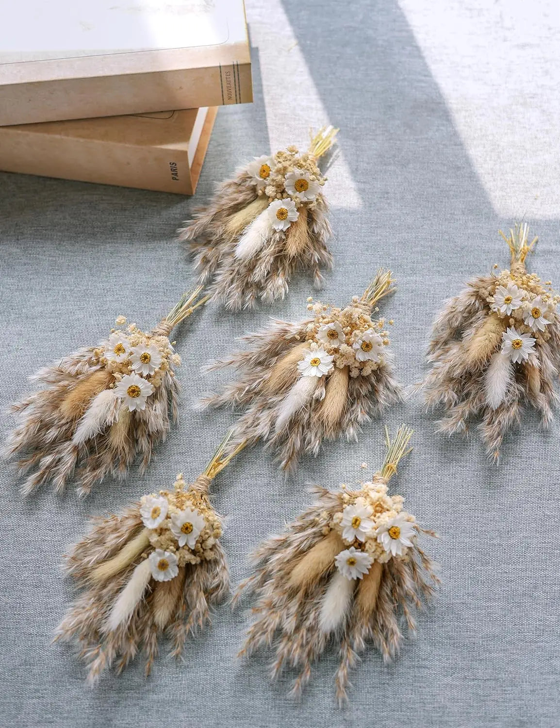Group of dried flower boutonnieres with tan pampas, white daisies, and ribbon-wrapped stems