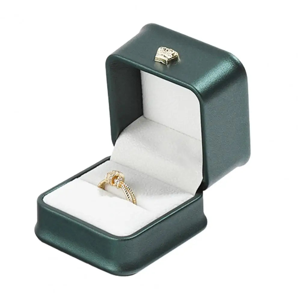 Dark green ring box with open lid, gold crown clasp, and ring on white cushion