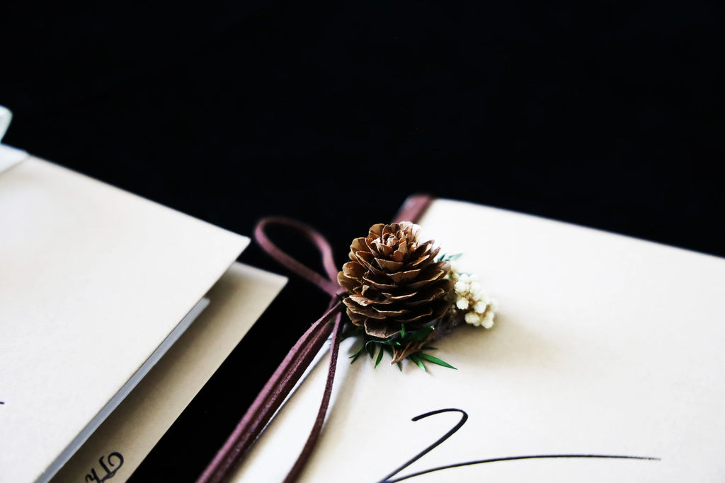 Close-up of ivory wedding vow booklet with gold “Vows” and pinecone-style floral ornament