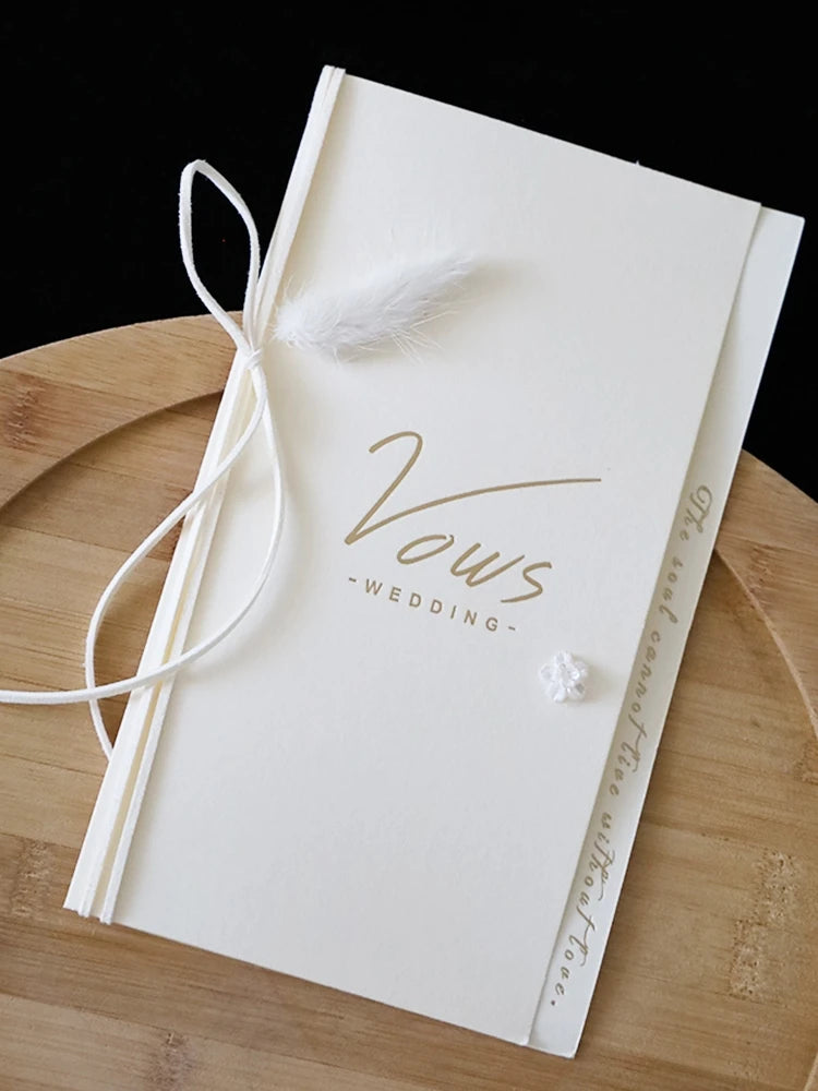 Ivory vow booklet with gold foil “Vows” on cover, tied with white ribbon bow