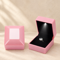 Pink LED proposal ring box with open lid and ring on black velvet insert.